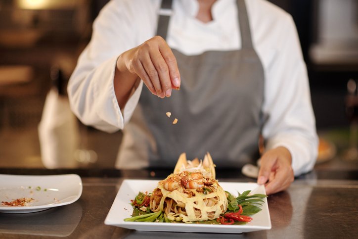 Cook garnishing shrimp pasta with crushed smoked peanuts