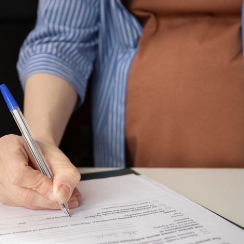 Pregnant woman signing an insurance form for maternity coverage, prenatal care, and childbirth expenses