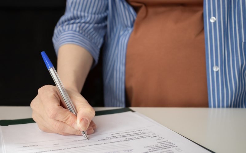 Pregnant woman signing an insurance form for maternity coverage, prenatal care, and childbirth expenses