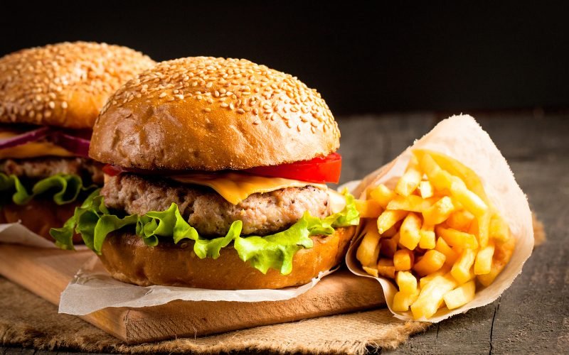 Close-up photo of home made hamburger with beer made of beef, onion, tomato, lettuce, cheese and spices. Fresh burger closeup on wooden rustic table with potato fries and chips.