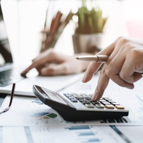 Close up Business woman using calculator and laptop for do math finance on wooden desk in office and business working background, tax, accounting, statistics and analytic research concept