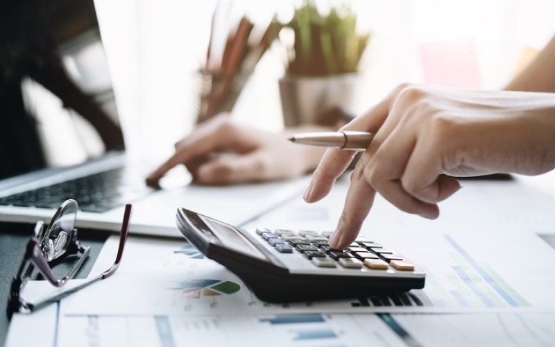 Close up Business woman using calculator and laptop for do math finance on wooden desk in office and business working background, tax, accounting, statistics and analytic research concept