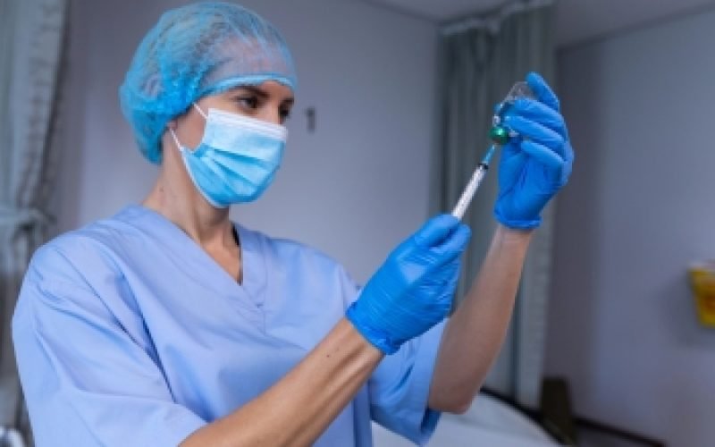 Caucasian female doctor in hospital wearing face mask holding syringe and preparing vaccination