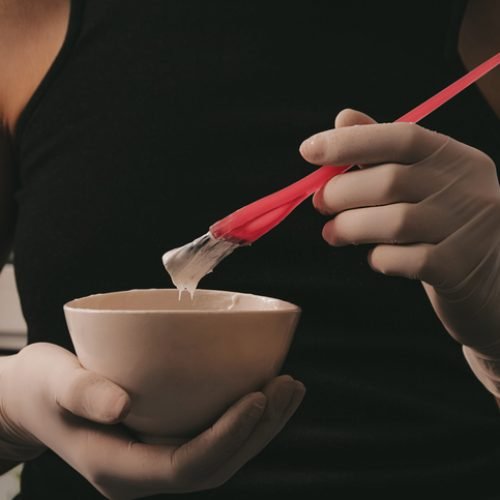 girl in white rubber protective gloves holding a brush in her hands and stirring hair dye close-up colorist hair care at home hair mask