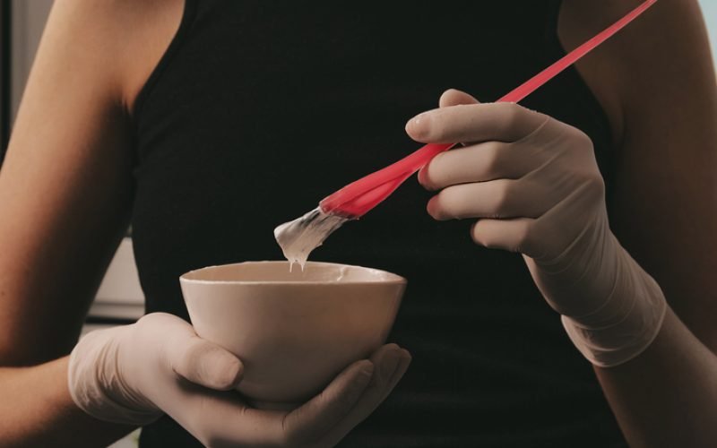 girl in white rubber protective gloves holding a brush in her hands and stirring hair dye close-up colorist hair care at home hair mask