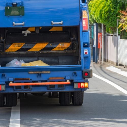 The photo captures the rear view of a garbage truck as it operates within a city environment. This might include details of the truck's mechanisms, collected waste, or the urban surroundings.