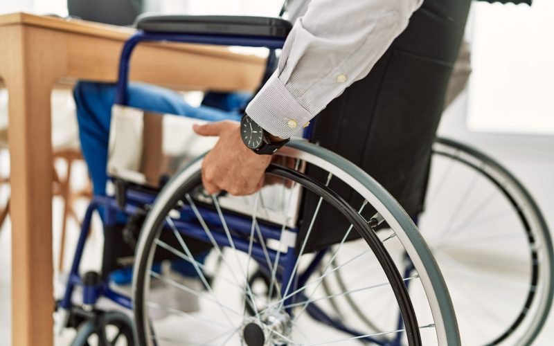 Middle age grey-haired man business worker sitting on wheelchair working at office
