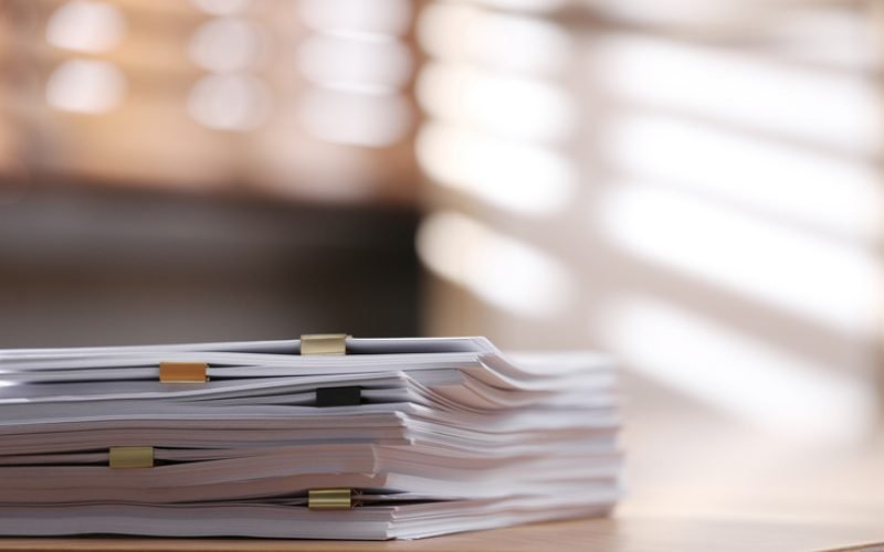 Stack of blank paper with binder clips on wooden table indoors. Space for text
