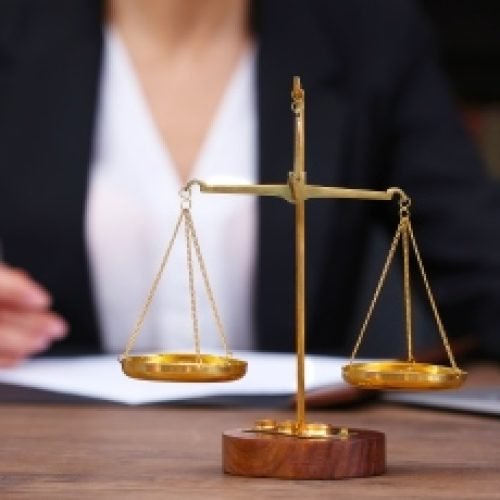 Scales of justice on wooden table and female lawyer on background