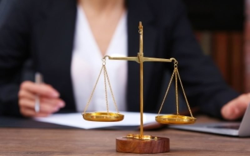 Scales of justice on wooden table and female lawyer on background