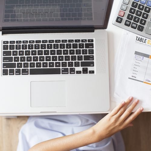 Cropped view of business woman hands making notes on document with table and working on laptop computer on desk. Top view.