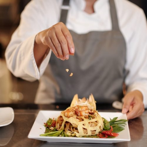 Cook garnishing shrimp pasta with crushed smoked peanuts