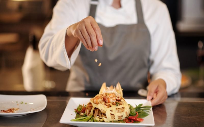 Cook garnishing shrimp pasta with crushed smoked peanuts