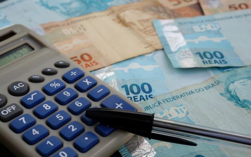 Finance Concept - Calculator, Brazilian Money and Pen on black background.