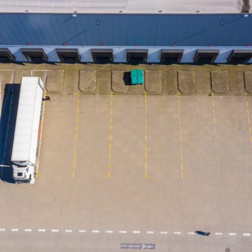 Aerial view of goods warehouse. Logistics center in industrial city zone from above. Aerial view of trucks loading at logistic center