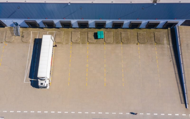 Aerial view of goods warehouse. Logistics center in industrial city zone from above. Aerial view of trucks loading at logistic center