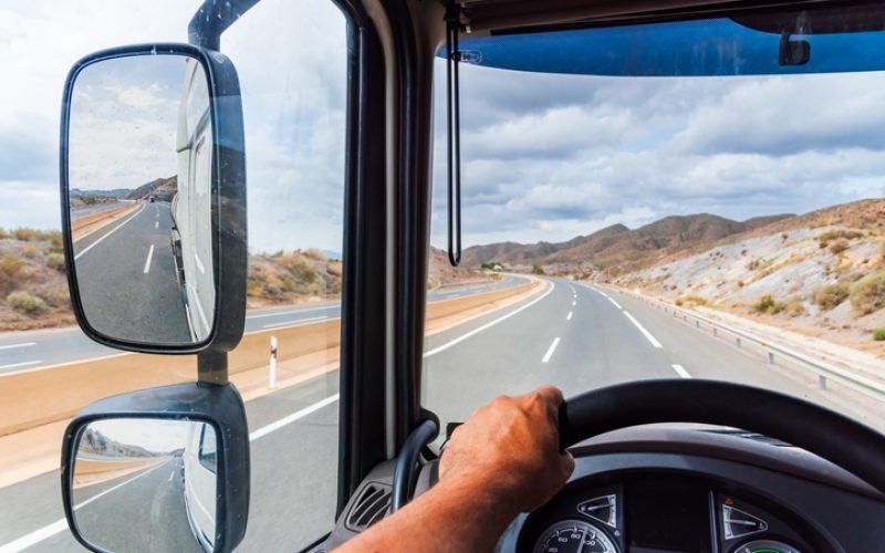 View from the driving position of a truck of the rearview mirror and the empty highway.