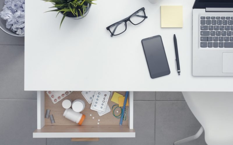 Open work desk drawer containing many different medicines and drugs: healthcare and addiction concept, copy space