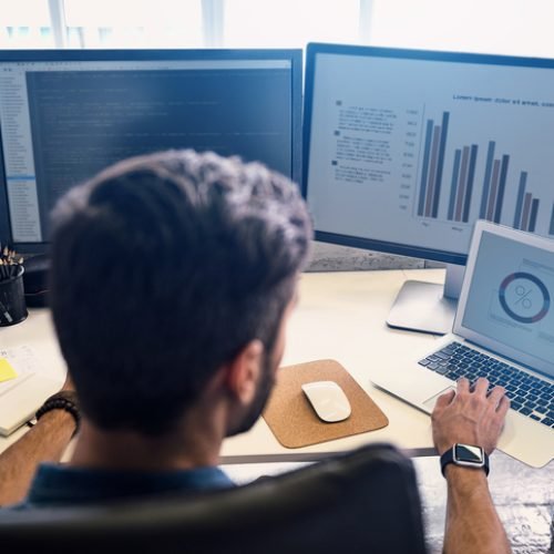Man creating statistics in modern office. He working on digital devices while sitting at table and turning back to camera